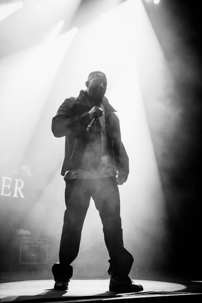 Dynamic black and white image of a rapper performing live onstage with striking lights.